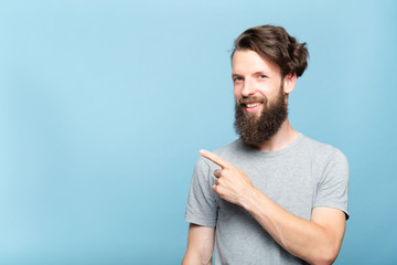 smiling young hipster man pointing sideways with index finger. copy space for text or product...