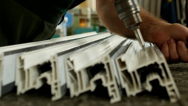Production of pvc windows, the worker screws a metal profile to the plastic profile of the pvc window section, manufacturing of plastic windows