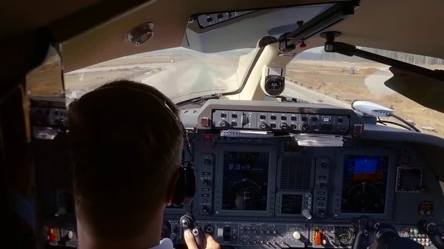 professional airman is landing an aircraft on airstrip in sunny day in summer, view from cabin
