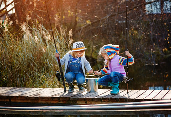 Two little girls with fishing rods, sitting on a wooden pontoon and bragging of caught fish