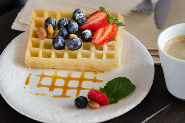Close up of Belgian waffles  decorated with strawberries, blueberries ,almond,  icing sugar and caramel. Delicious homemade dessert  for breakfast.