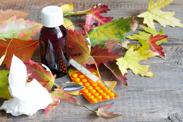 Pills medicine and thermometer with autumn leaves cold and flu treatment concept