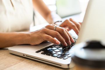 Closeup woman's hands typing on a laptop that is on a wooden desk