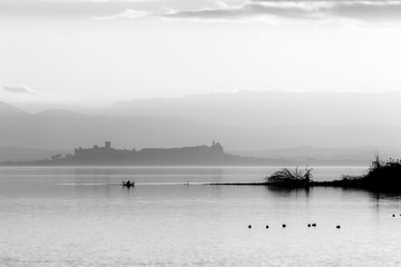 Obraz na płótnie Canvas Beautiful view of Trasimeno lake at sunset with birds on water, a man on a canoe and Castiglione del Lago town in the background