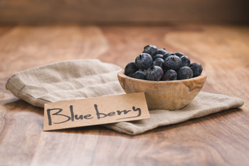 Fresh blueberries in wood bowl on table with paper card slightly toned