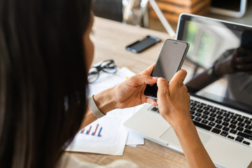 Typing business message. Close-up of young woman in formalwear holding mobile phone while sitting at her working place.