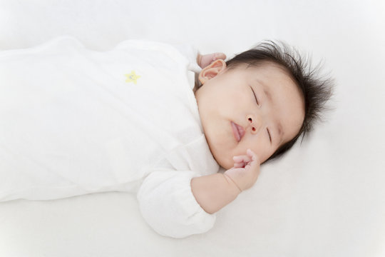 白いオーバーオールを着て眠る生後3ヶ月になった新生児。新生児、赤ちゃん、育児、健康のイメージ