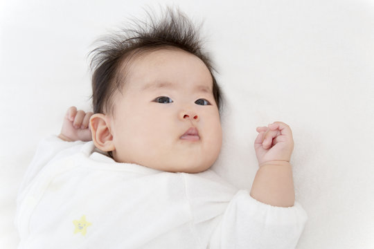 白いオーバーオールを着てカメラ目線の生後3ヶ月になった新生児。新生児、赤ちゃん、育児、健康のイメージ