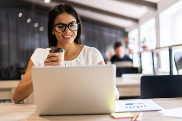 New solution every day. Confident young woman in smart casual wear working on laptop while sitting at her working place in office.