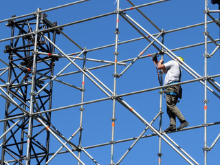 Construction worker working on scaffolding. Steeplejack on the background of clear blue sky