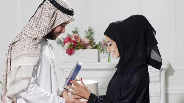Arabic man Giving Gift Box to Woman. Young Couple Relaxing Indoor. Romantic Relationship Concepts.