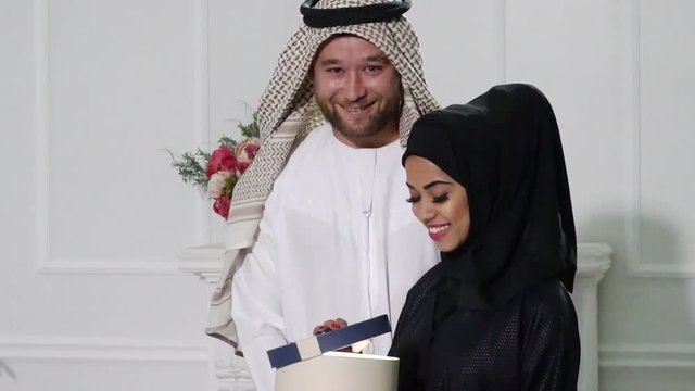 Arabic man Giving Gift Box to Woman. Young Couple Relaxing Indoor. Romantic Relationship Concepts.