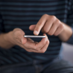 Squared image of young caucasian man using apps on a touchscreen smartphone - Hands close-up focus on phone - Concept for using technology, shopping online, using mobile apps, texting, phone addiction