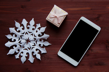 New Year's Christmas concept. Snowflake made of paper, box gift and a smartphone on a wooden table