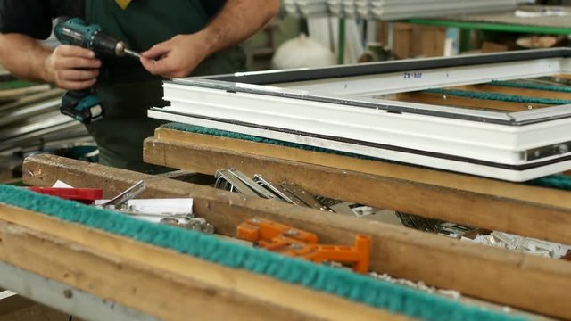 Production and manufacturing of pvc windows, the male worker assembles a pvc profile window, fastens the hinged parts, pvc window, screwdriver pvc window assembly