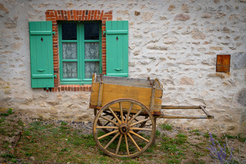 Obraz premium Window with green shutters and an old wooden wheelbarrow in Montrol-Senard, France.