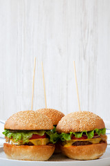Cheeseburgers on grey plate. White wooden background. Side view. Closeup.