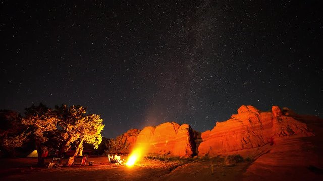 Time lapse of campsite in the Utah desert at night viewing red rock lit up by campfire and stars moving through the sky.