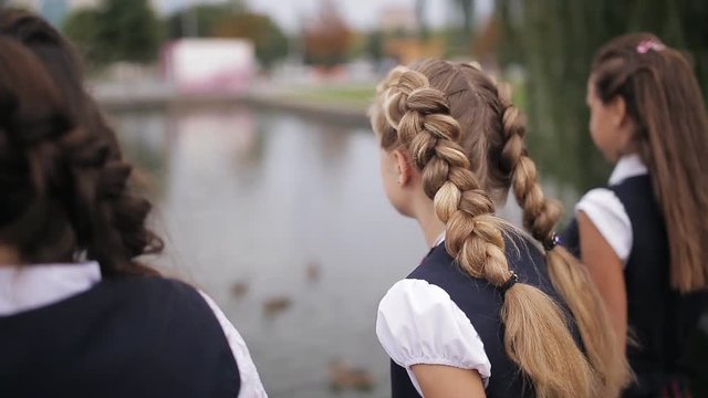 Students in school uniform feeding ducks in a pond in the school yard. Girls College coeds wearing the same school uniform feed the ducks in the pond on campus