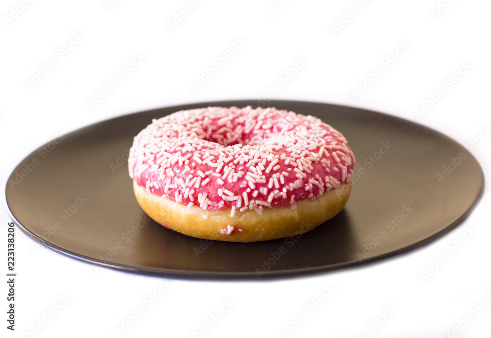 Wall mural brightly pink donut on a black ceramic plate on white background.