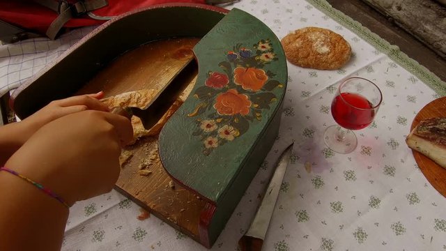 Close detail on a teenager dressed in typical Tyrolean dress, cut dry bread with a typical Tyrolean bread cut