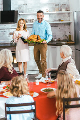 young man and woman carrying wine and turkey for thanksgiving dinner with family at home