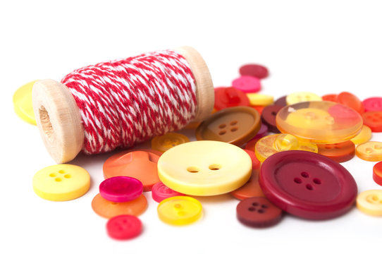 closeup of red and orange buttons and red cotton yarn on white background
