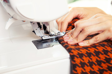 Young woman working in a sewing studio: sewing with a serger, overlocker. Fashion designers atelier   