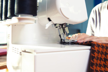 Young woman working in a sewing studio: sewing with a serger, overlocker. Fashion designers atelier   