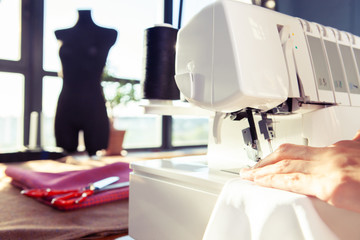 Young woman working in a sewing studio: sewing with a serger, overlocker. Fashion designers atelier   