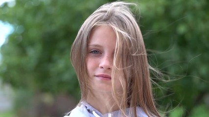 Beautiful blond young girl with freckles outdoors looking, hair blowing in wind on nature background, close up portrait, slow motion