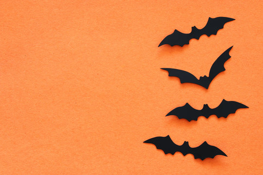 Halloween holiday concept. Black bats over orange background. Top view, flat lay.
