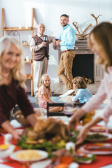 young and adult men spending time with kids while women serving thanksgiving day table
