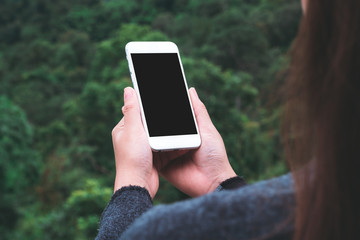 Mockup image of a woman holding white smart phone with blank desktop screen in outdoor with blur green mountains background