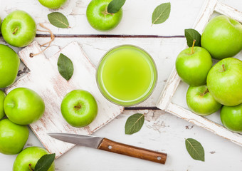 Glass of fresh organic apple juice with granny smith green apples in box on wooden background with knife