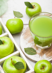 Glass of fresh organic apple juice with granny smith green apples in box on wooden background