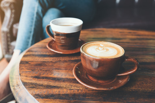 Closeup image of two cups of hot latte coffee and black coffee on vintage wooden table in cafe