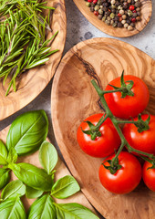 Organic Cherry Sugardrop Tomatoes on the Vine with basil in oilve wood plate and spoon with pepper on white kitchen background.