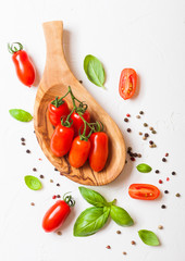 Organic Mini San Marzano Tomatoes on the Vine with basil and pepper in oilve wood plate on white kitchen background.