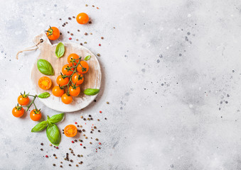 Organic Cherry Orange Rapture Tomatoes on the Vine with basil and pepper on chopping board on stone kitchen background. Space for text