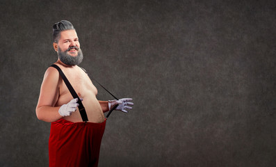 Santa Claus with a naked belly with suspenders smiles against the background of the copyspace.
