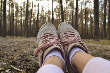 A female feet in sneakers against a forest background. A girl relaxing in the forest.