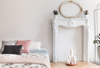 An English style bedroom interior with pastel pillows and rose pattern cover on the bed. White ornamented fireplace portal beside the bed. Copy space wall. Real photo.
