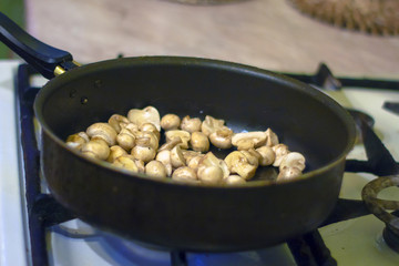 A woman is frying mushrooms in the kitchen. The process of frying in a frying pan. Preparation of food by prescription. Home kitchen. Mom cooks fried mushrooms in a frying pan