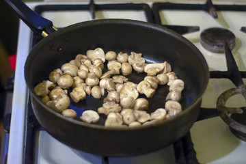 A woman is frying mushrooms in the kitchen. The process of frying in a frying pan. Preparation of food by prescription. Home kitchen. Mom cooks fried mushrooms in a frying pan