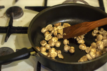 A woman is frying mushrooms in the kitchen. The process of frying in a frying pan. Preparation of food by prescription. Home kitchen. Mom cooks fried mushrooms in a frying pan