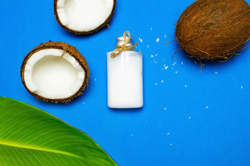 Organic cosmetics with coconut oil, ripe coconut on blue colored background top view minimal flat lay style. Coconut shavings, oil, milk. Healthy skincare. Homemade cosmetic for peeling and spa care.