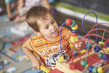 Little Asian child playing with lots of colorful plastic blocks indoor. Kid boy wearing colorful shirt and having fun with building and creating.