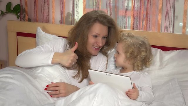 caucasian little girl and mother with tablet computer on bed