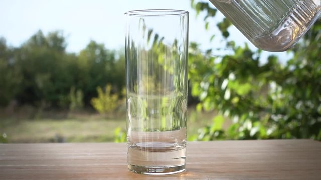 Pouring glass of water on blurred garden background in slow motion fullHD real video